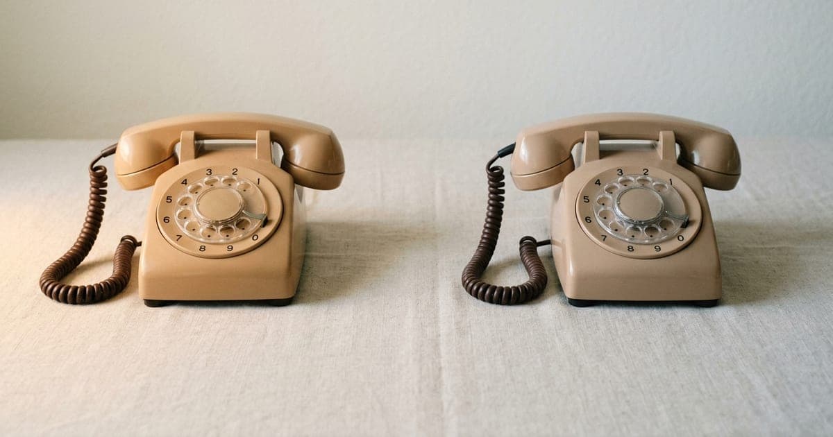 Two desk telephones side by side on a plain surface
